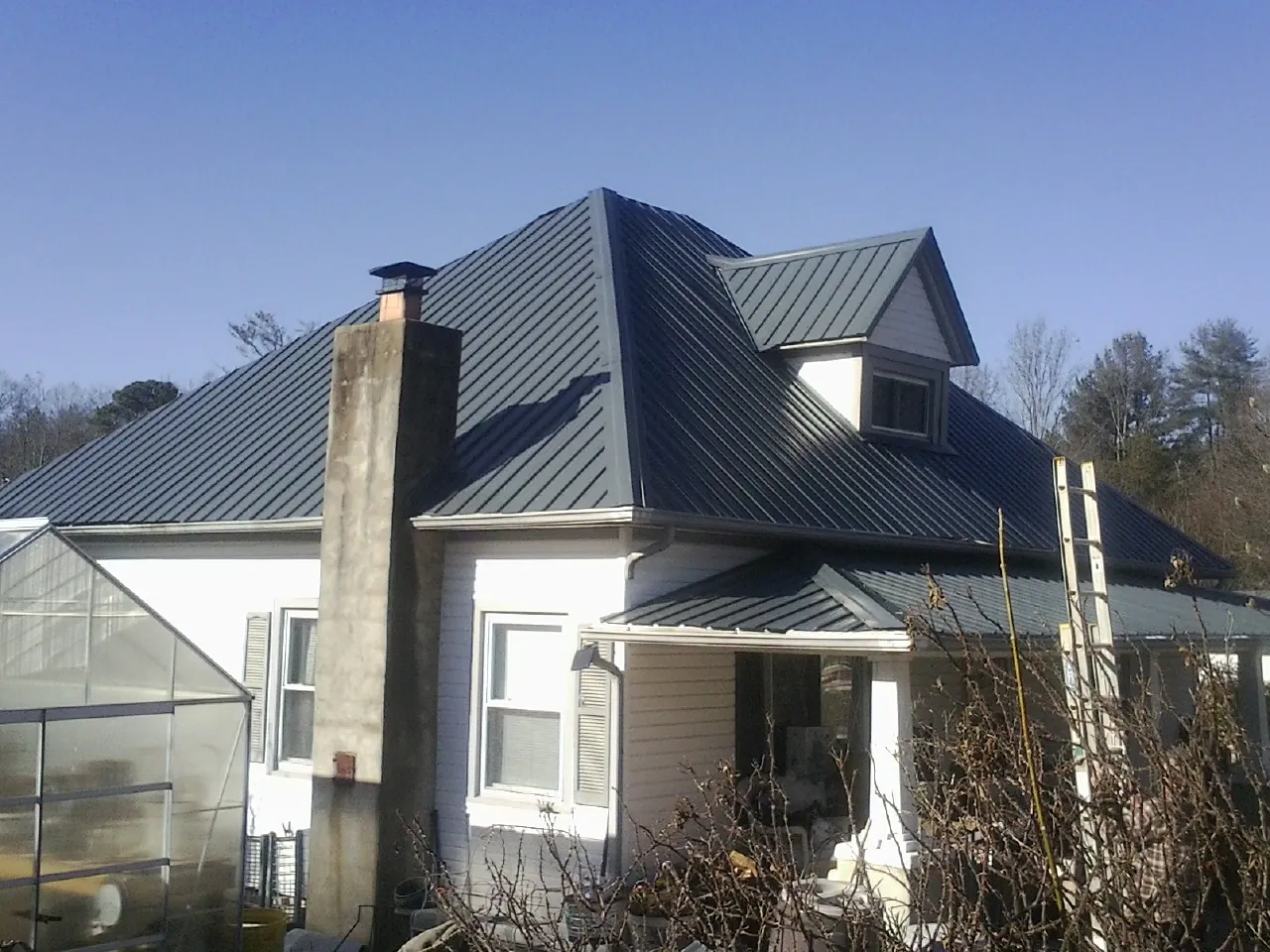 Dark blue standing seam metal roof on a white farmhouse with dormer — Slate & Tile Roof Repair by Roofing Brothers in Acton