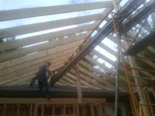 Rafters going up over a new addition with a worker on the wall in Acton
