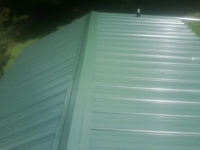 New green metal panels meeting at the ridge of a roof — Flat Roof Repair work by our crew in Acton