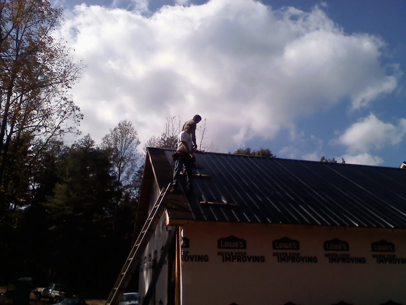 Roofer fastening dark metal panels high against a cloudy sky, from a Roof Inspection job in Acton